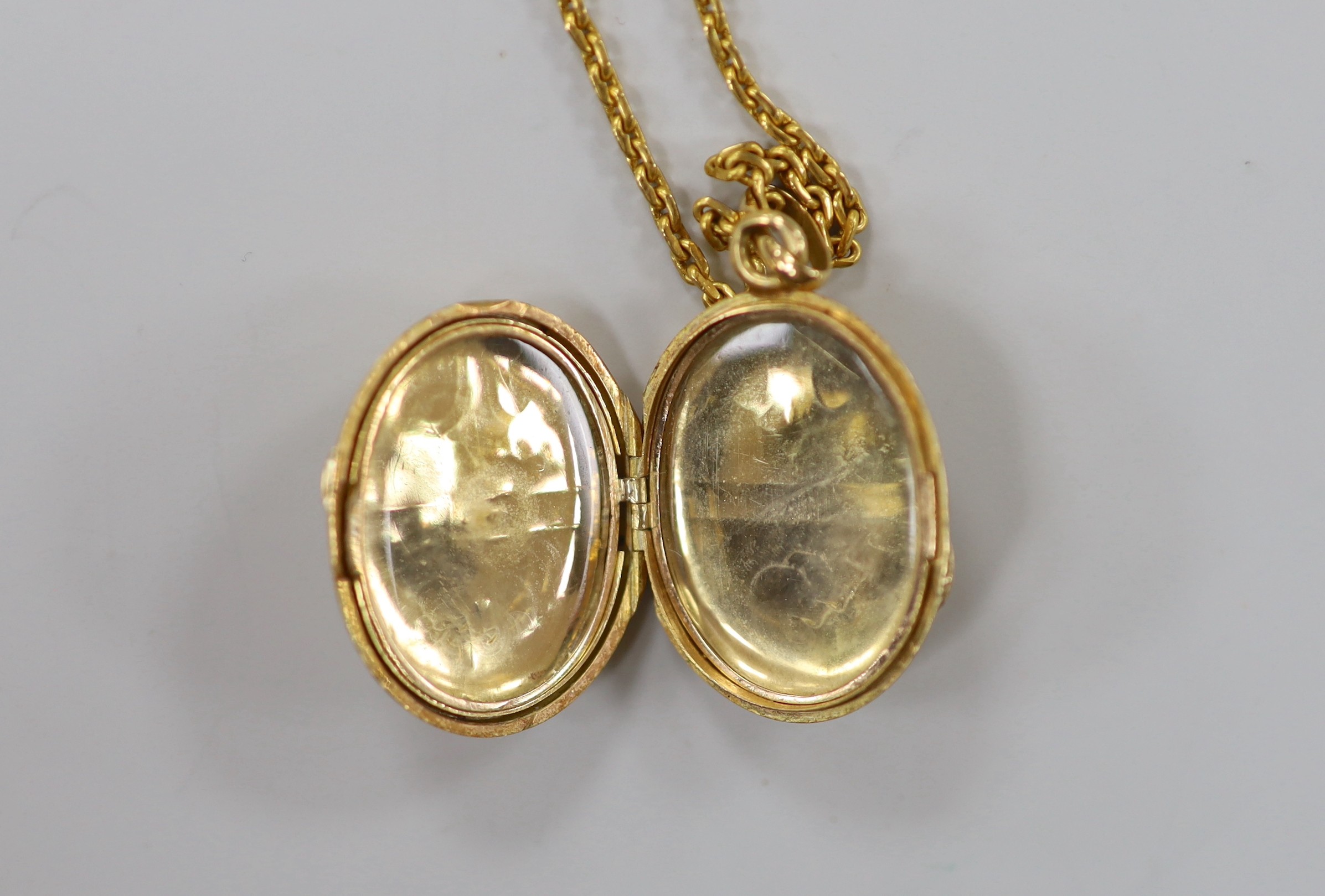 A continental engraved yellow metal oval locket, overall 38mm, on a 9ct chain, 47cm, gross weight 18.9 grams.